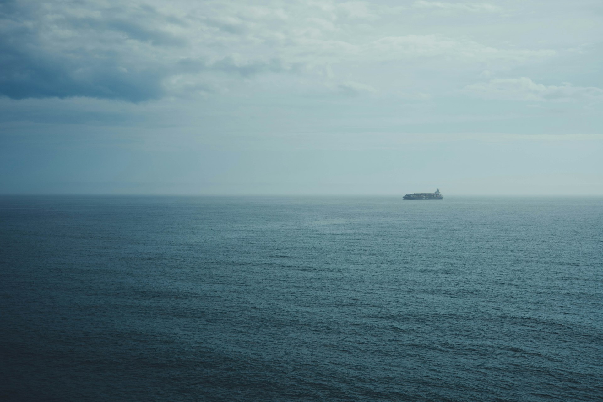 A lone cargo ship sails on a vast, calm ocean